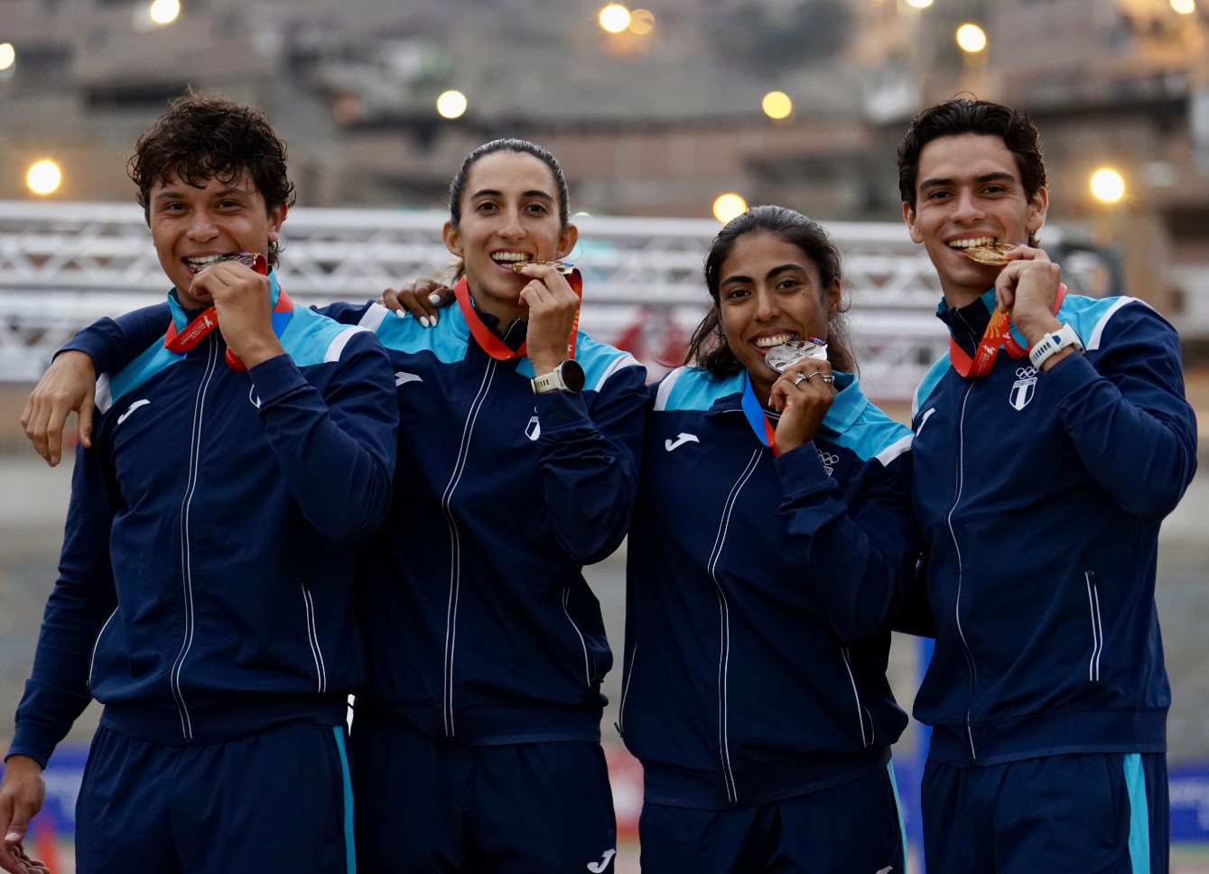 Cuatro atletas guatemaltecos muerden sus medallas con el uniforme de la delegación nacional
